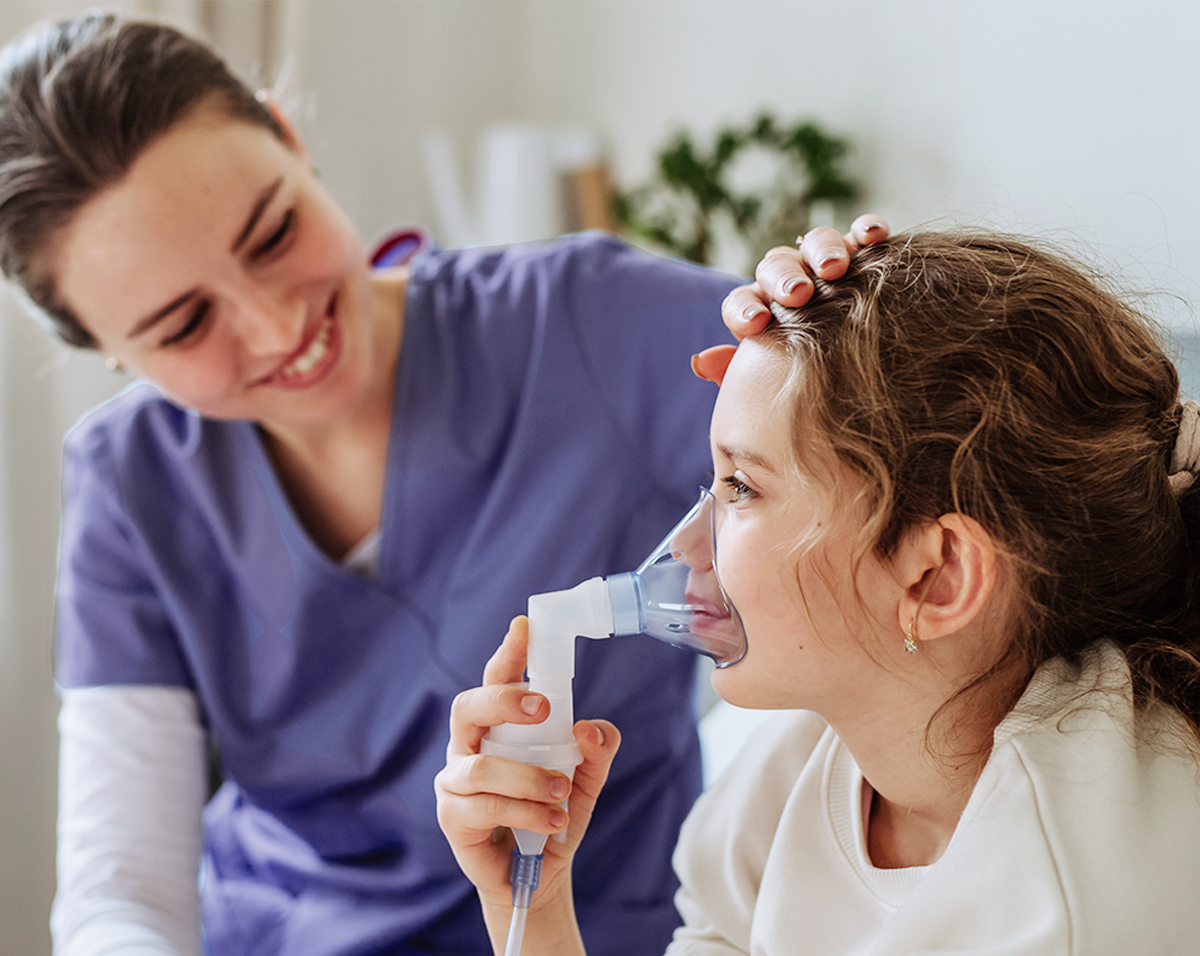 A specially-trained nurse administers a breathing treatment to a young child at home, part of At Home Healthcare's Private Duty Nursing program. The image captures a moment of compassionate care, with the child receiving medical attention in the comfort of their own home.