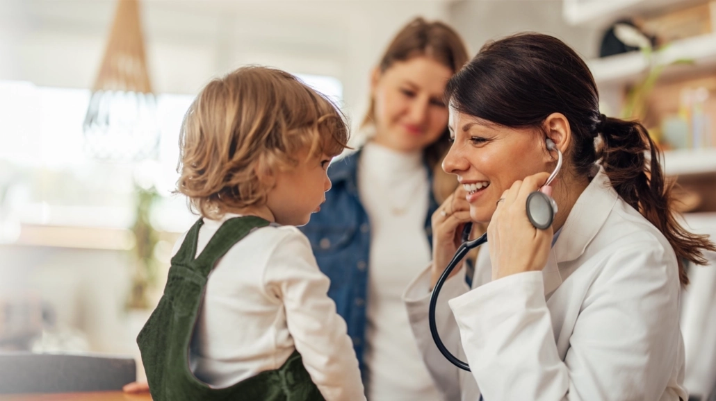 Friendly healthcare professional examining a young child at home.