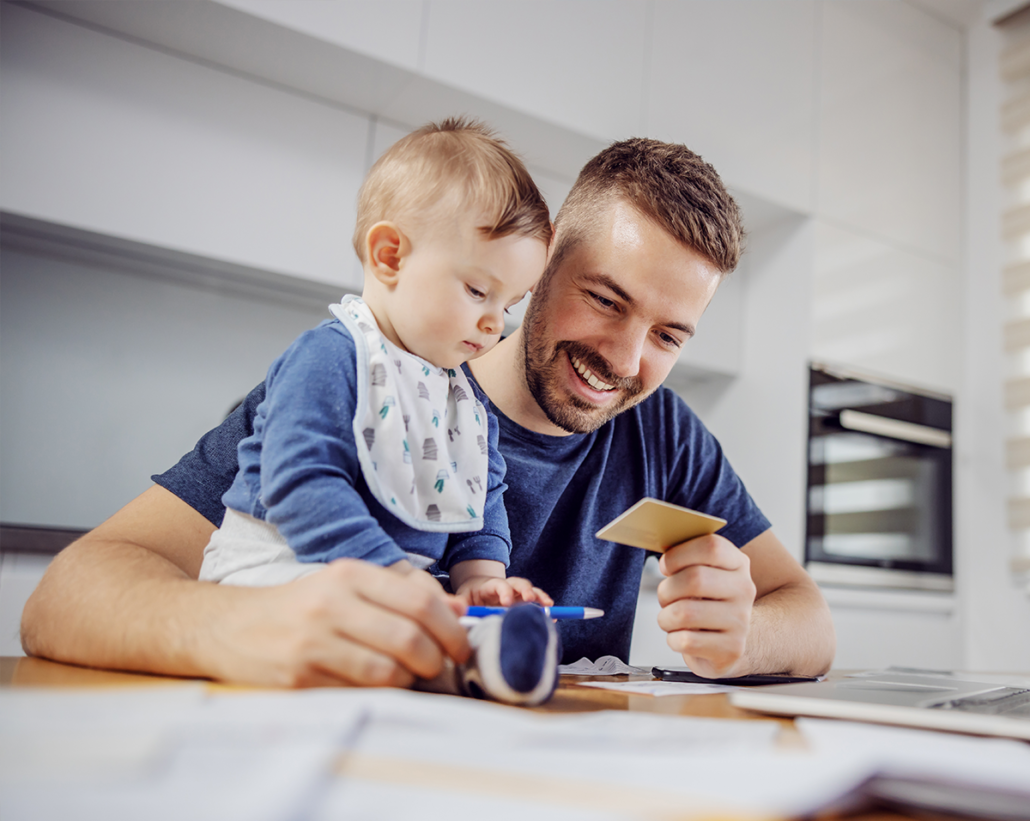 Image depicting a father holding a credit card while sitting with his young son, suggesting he is about to pay a bill. This scene highlights the convenience and family-focused approach of managing healthcare payments from home.